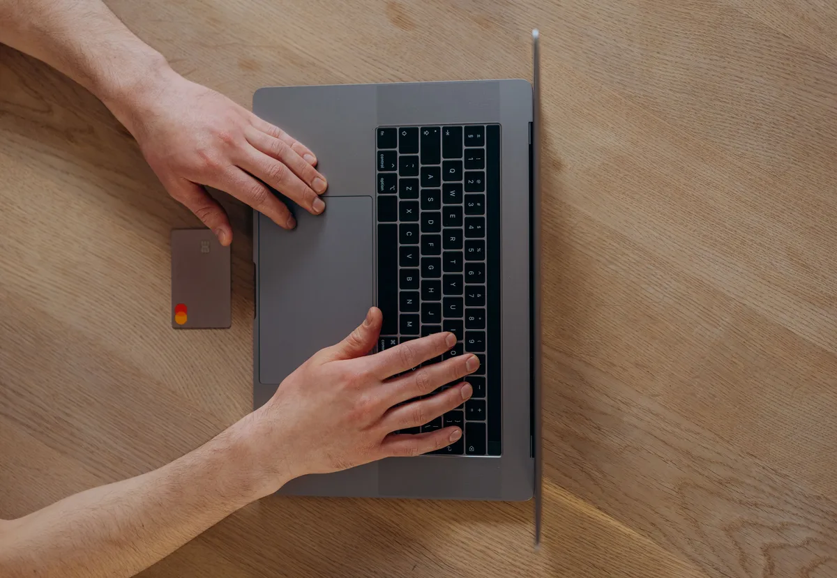 A laptop beside a credit card on a wooden table, the kind of checkout agentic AI commerce hands to an agent