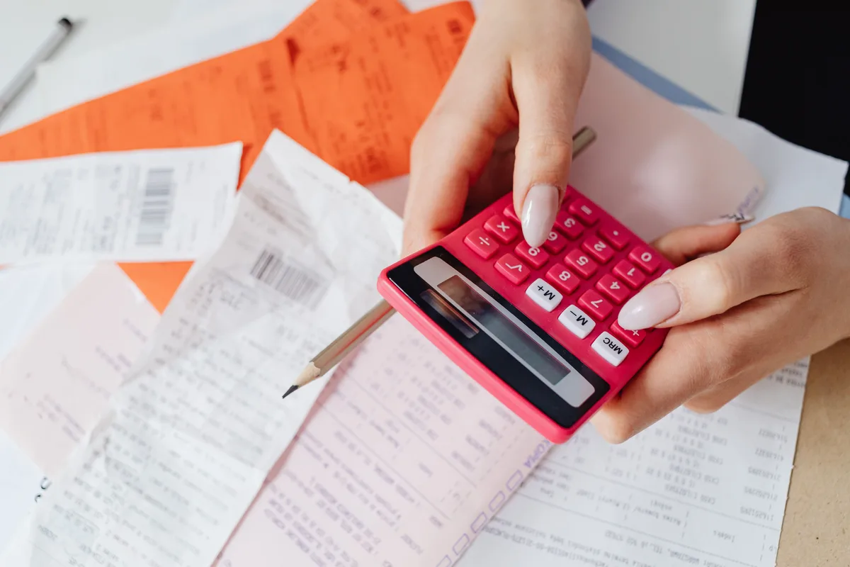 Hands using a pink calculator over a spread of paper receipts, like the arithmetic behind estimating an AI API bill per million tokens