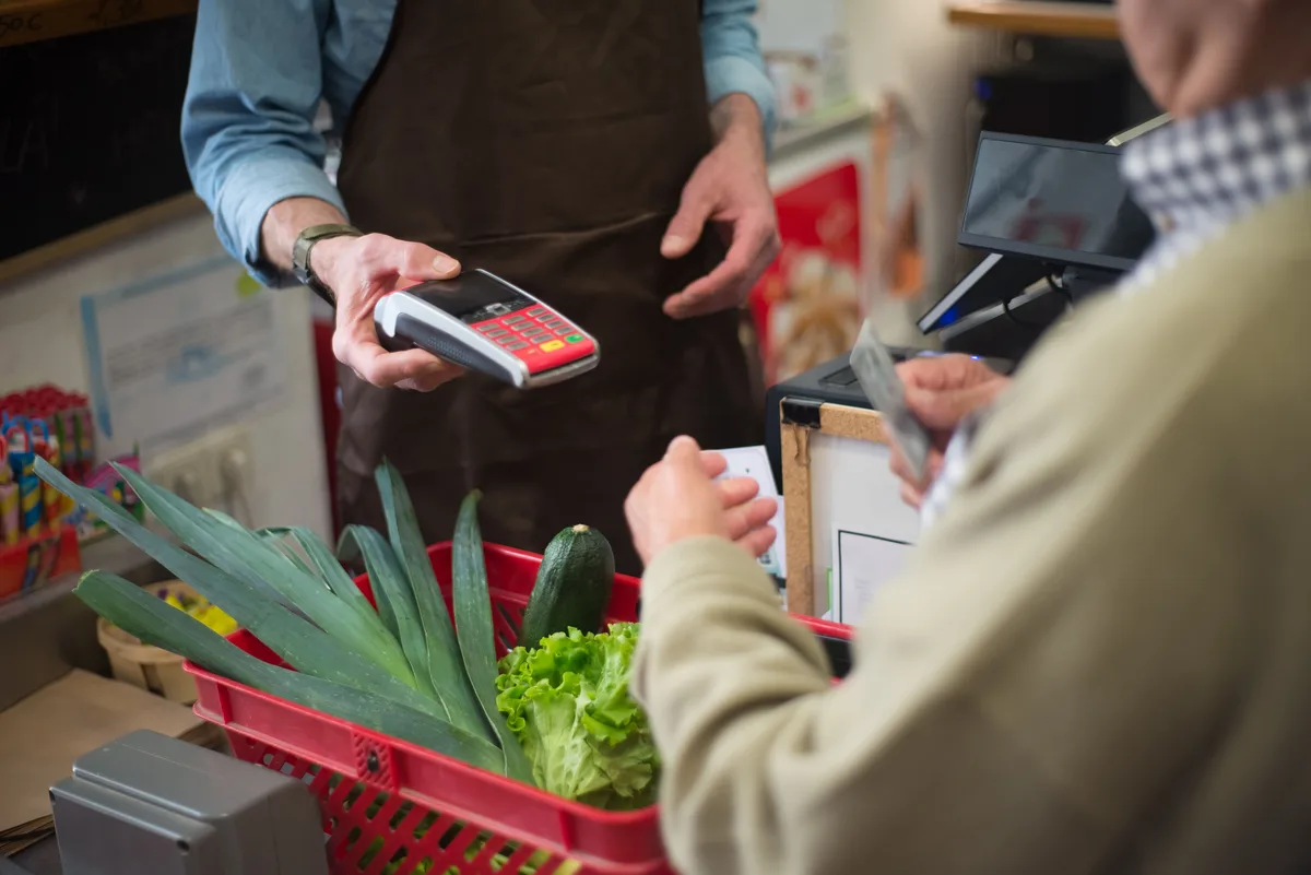 Customer paying for vegetables at a grocery checkout with a card, the point where SNAP benefits set by a caseworker reach a household