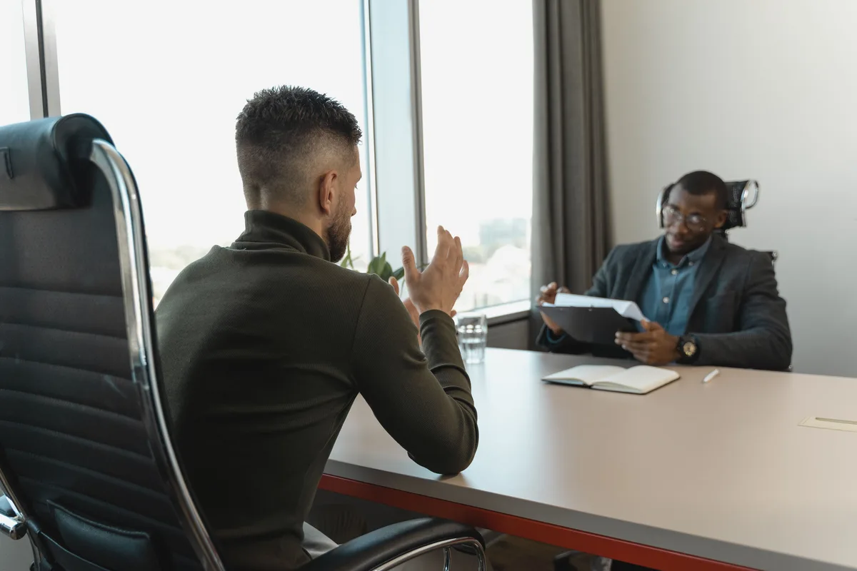 Two men in a job interview in a modern office, the kind of conversation where AI prompt engineer jobs are now won