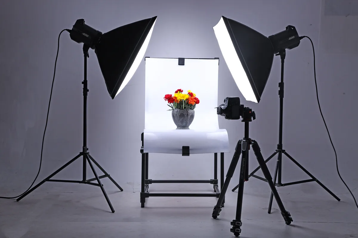 Photo studio with two softbox lights and a camera aimed at a vase of flowers, the kind of scene an AI image prompt example describes