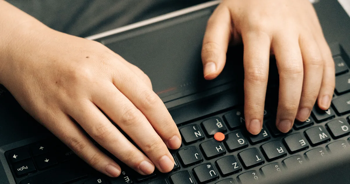 Close-up of hands typing on a black laptop keyboard, writing AI prompt examples