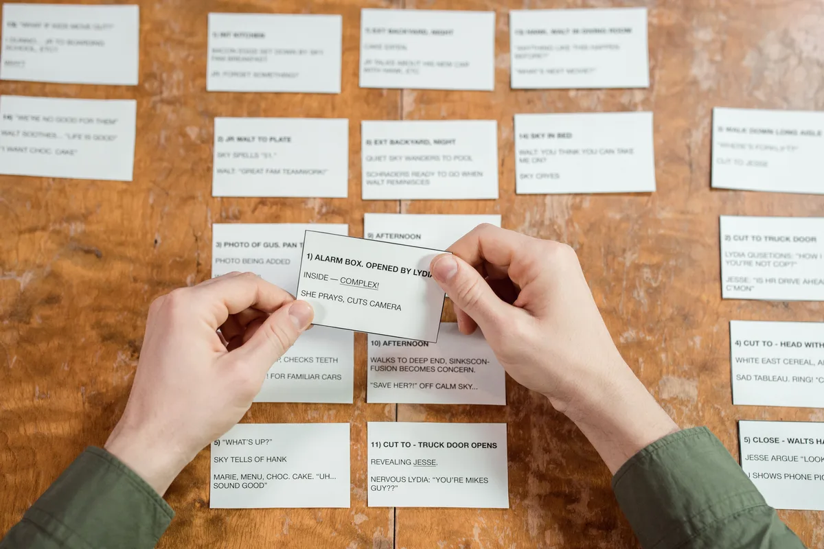 Hands arranging labelled index cards in rows on a wooden desk, like sorting entries in an AI prompt library by task