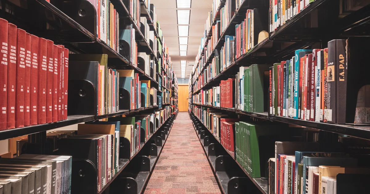 A long library aisle between full bookshelves, the kind of ordered collection an AI prompt library aims to be