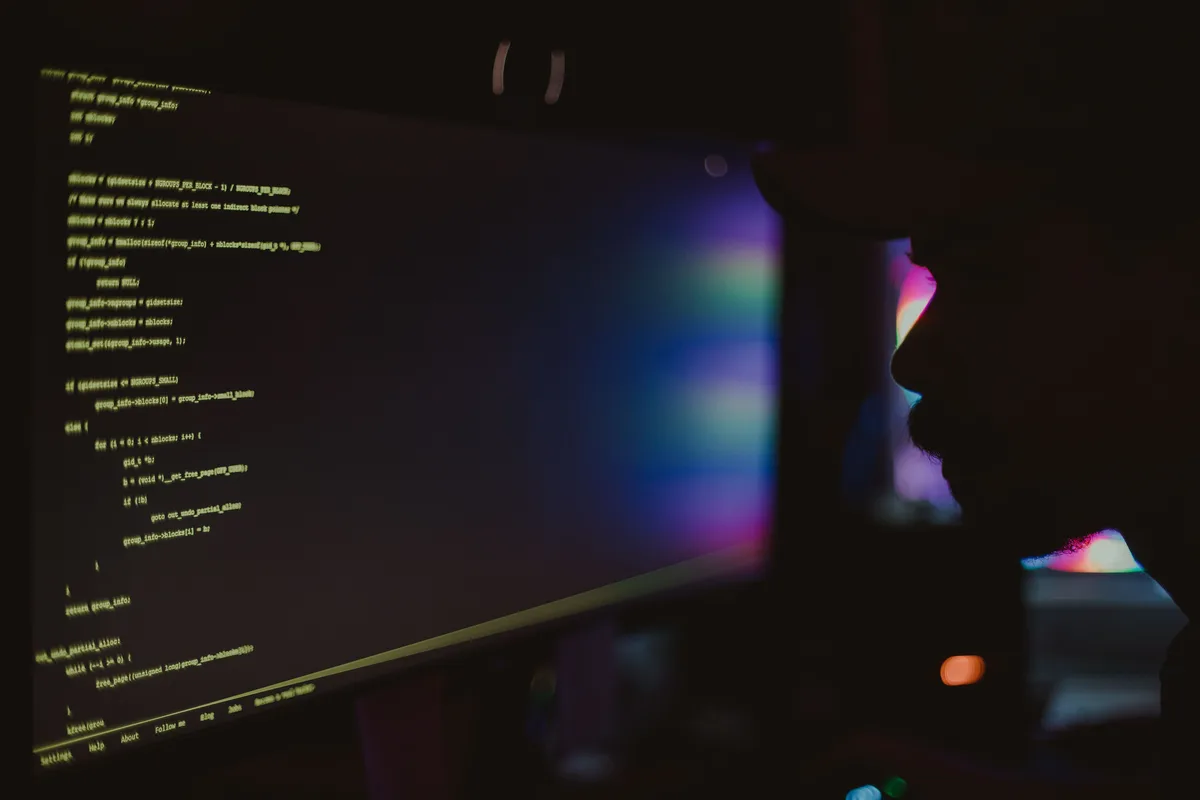 A programmer silhouetted against monitors of code at night, the review work that an autonomous AI software engineer leaves behind
