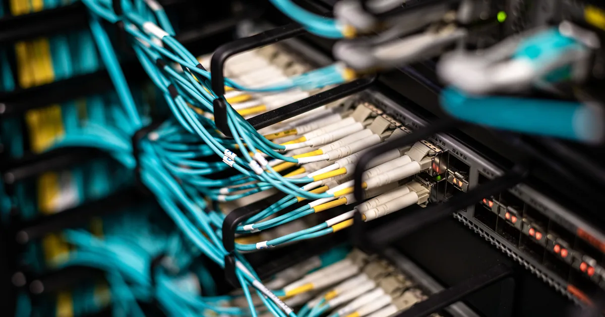 Dense bundles of network cables plugged into a data-centre patch panel, the surrounding infrastructure at the heart of the AI systems engineering problem