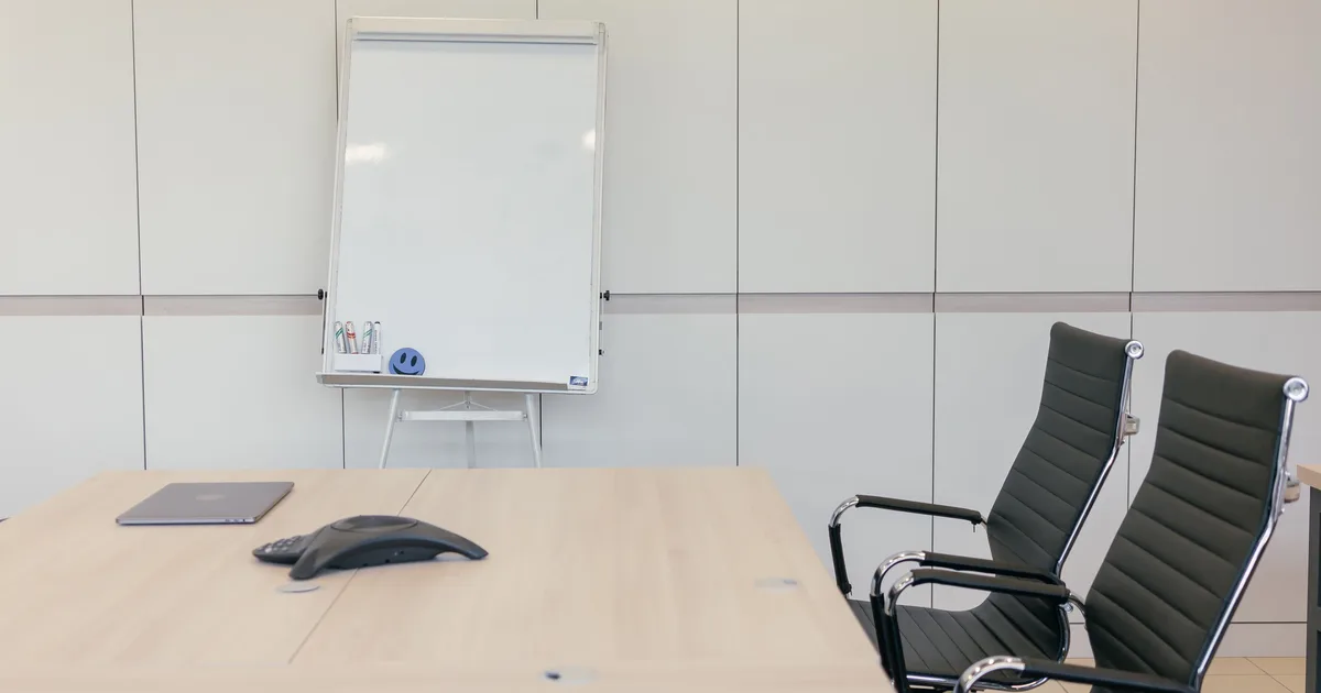 Empty conference room with a blank flipchart and two chairs, a picture of the AI transformation governance problem where no one has written down who decides