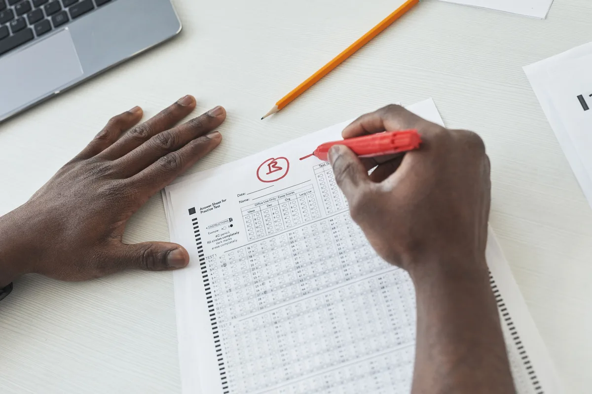 A teacher marking multiple-choice exams with a red pen, the scoring discipline a prompt test set needs