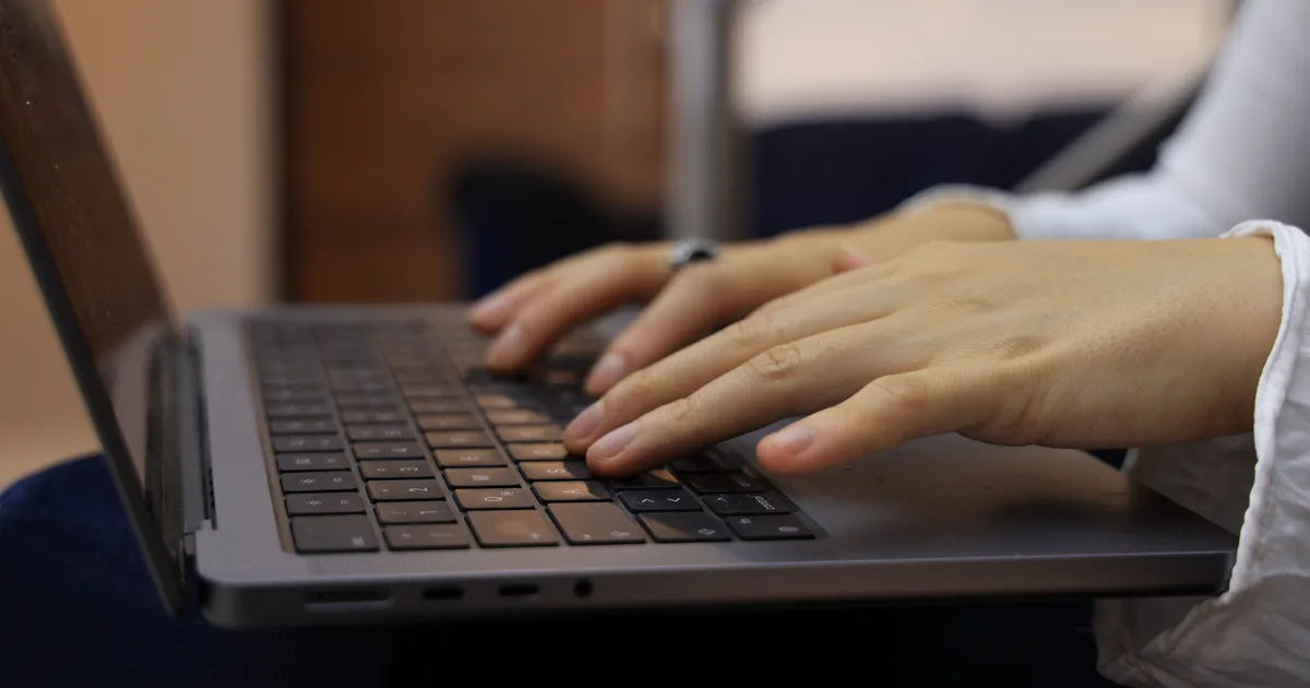 Hands typing on a laptop keyboard, the everyday work of training AI models with prompts