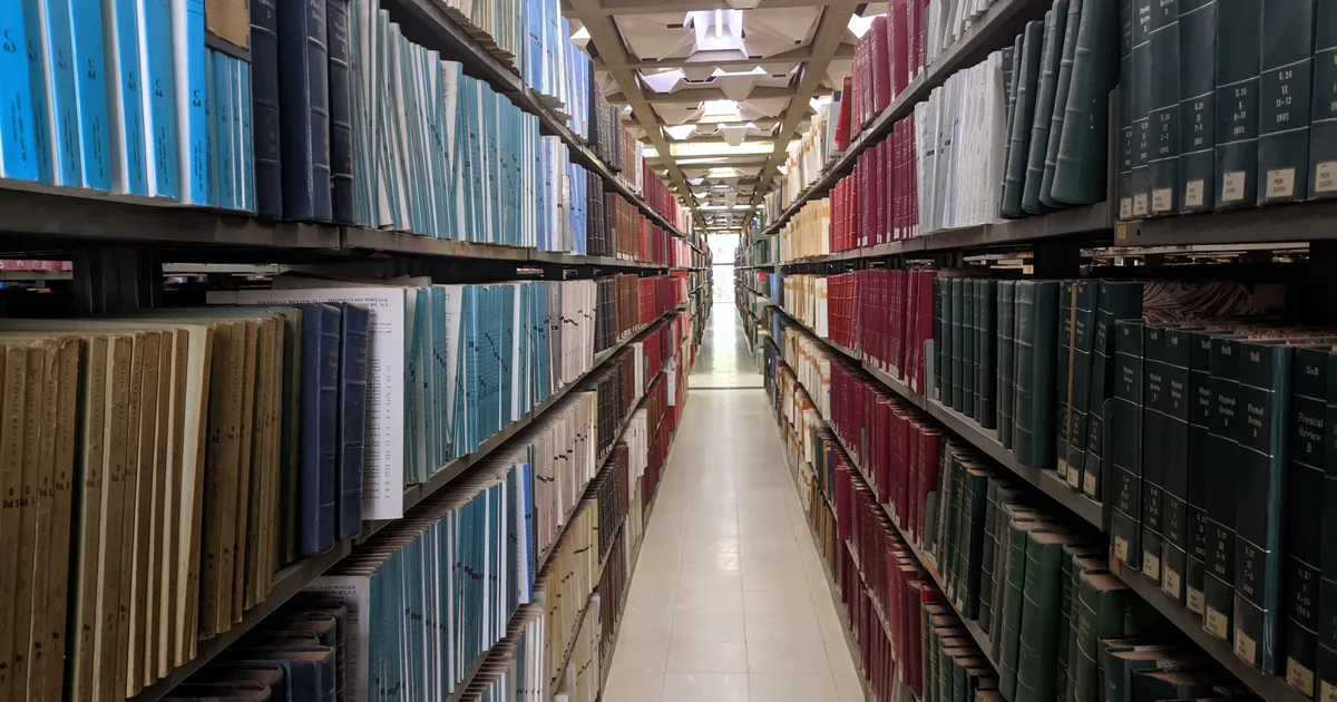 Long library aisle between shelves of bound volumes, illustrating a ranking of the best prompt engineering books in 2026