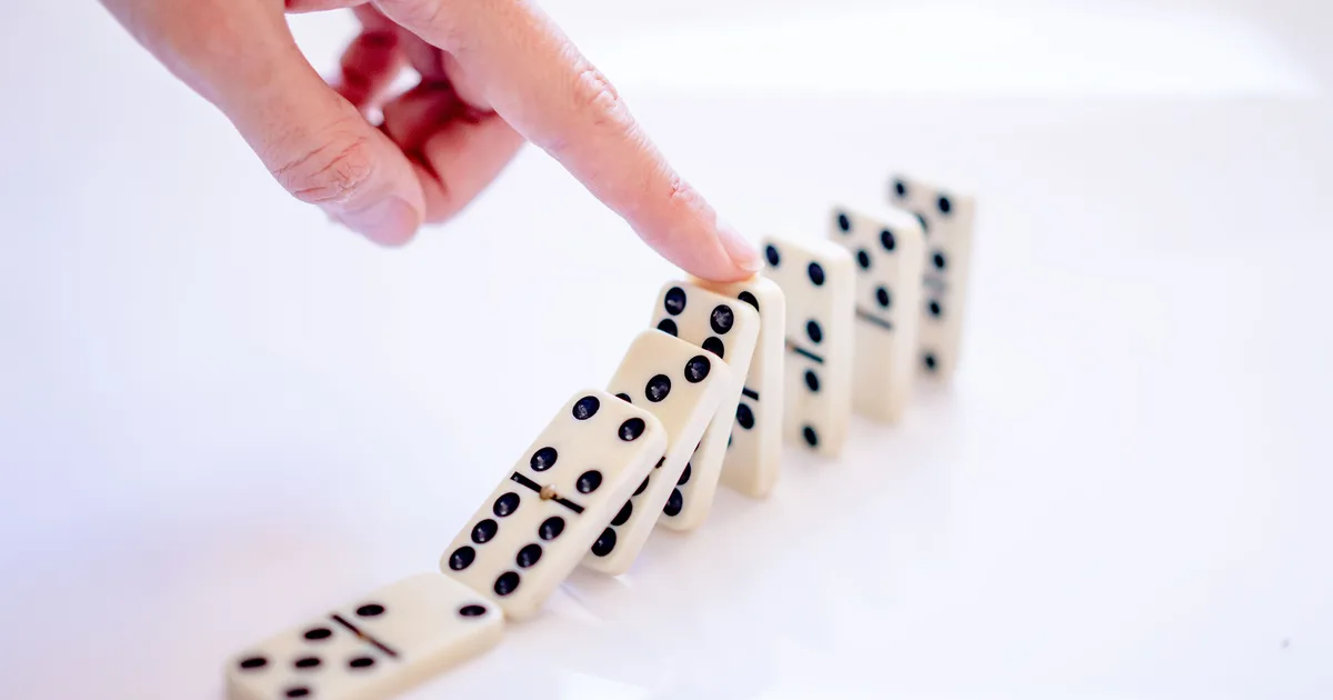 A hand tipping the first tile in a line of dominoes, the mechanism behind cause and effect AI prompts