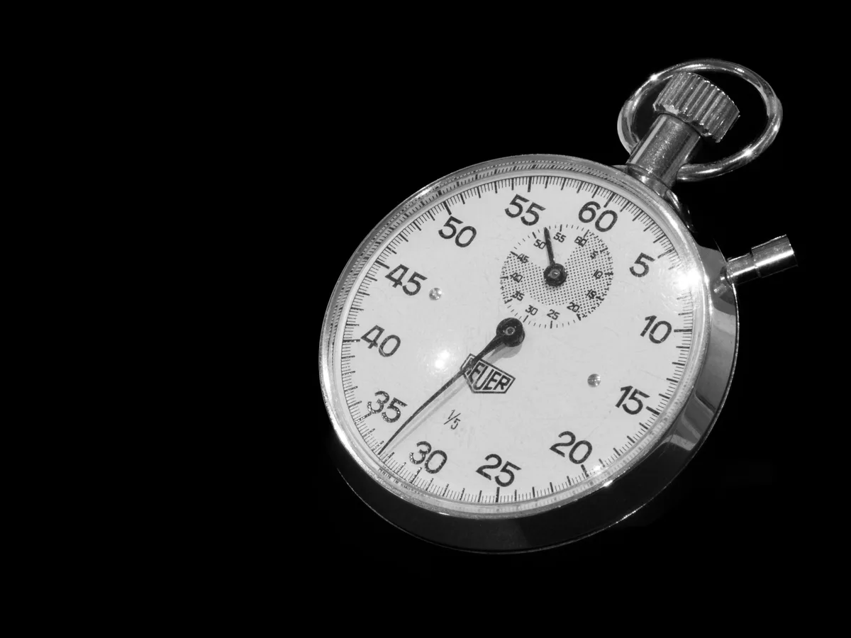 A vintage mechanical stopwatch with a black dial on a dark background, representing the reset timer behind Claude AI usage limits