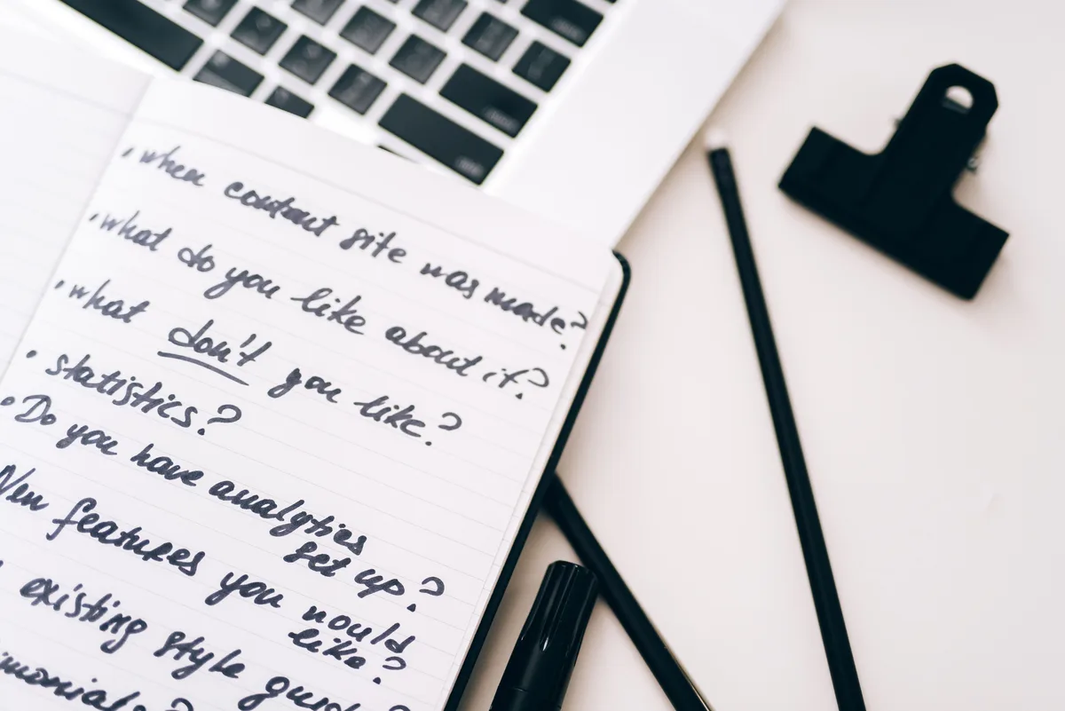 An open notebook of handwritten notes beside a laptop, the raw material that makes a Claude prompt produce writing detectors do not flag