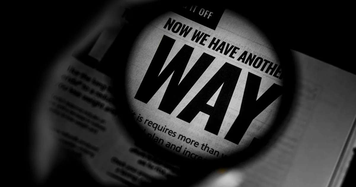 A magnifying glass enlarging a line of newspaper text in black and white, the way an AI detector inspects prose before flagging it