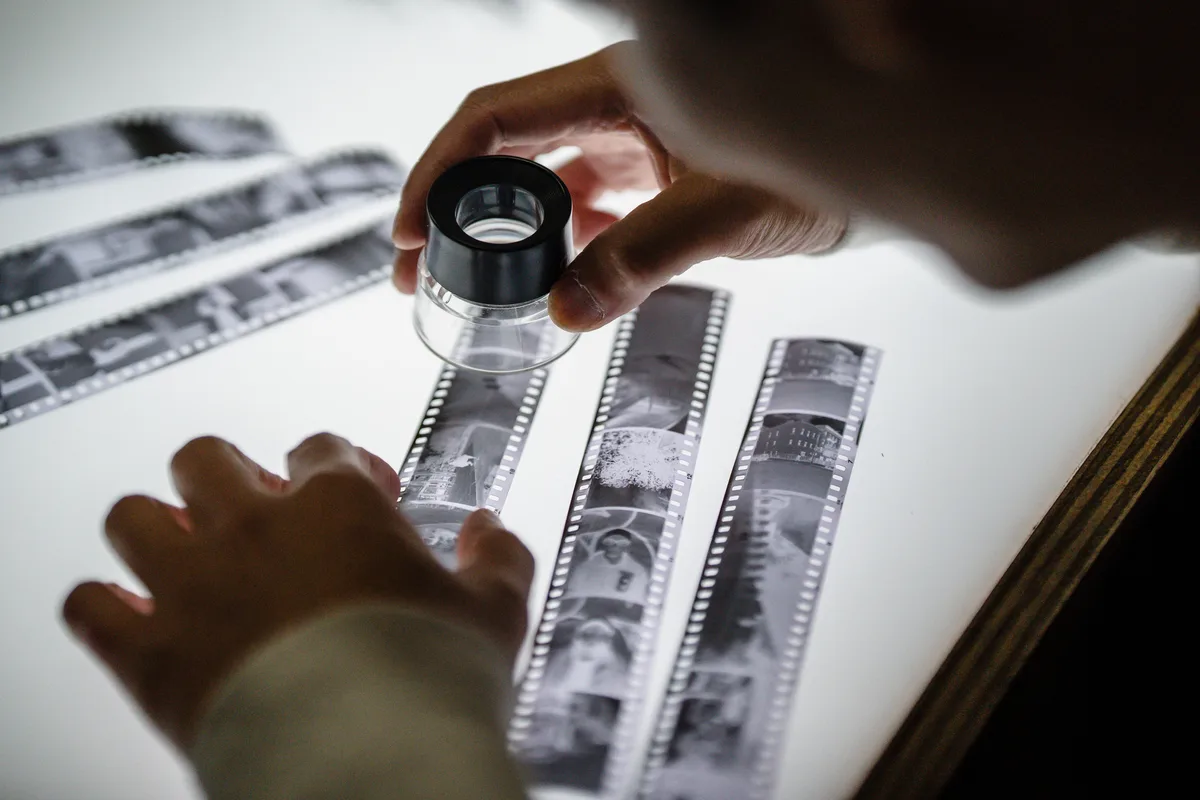 Hands examining film negatives with a magnifier on a light table, the same close reading an extracted AI prompt needs