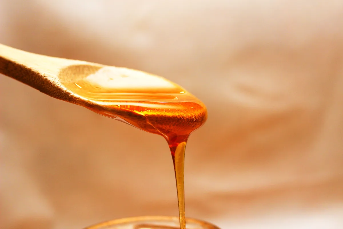 Macro shot of golden honey pouring from a wooden spoon, the kind of viscous subject that suits Grok AI prompts for slow motion