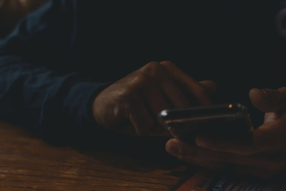 Hands scrolling a smartphone feed in a dim room, the kind of fast-moving X timeline that Grok AI search prompts point the model at
