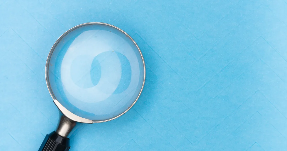 A magnifying glass on a blue surface, a stand-in for the narrow, targeted searches good Grok AI search prompts ask for
