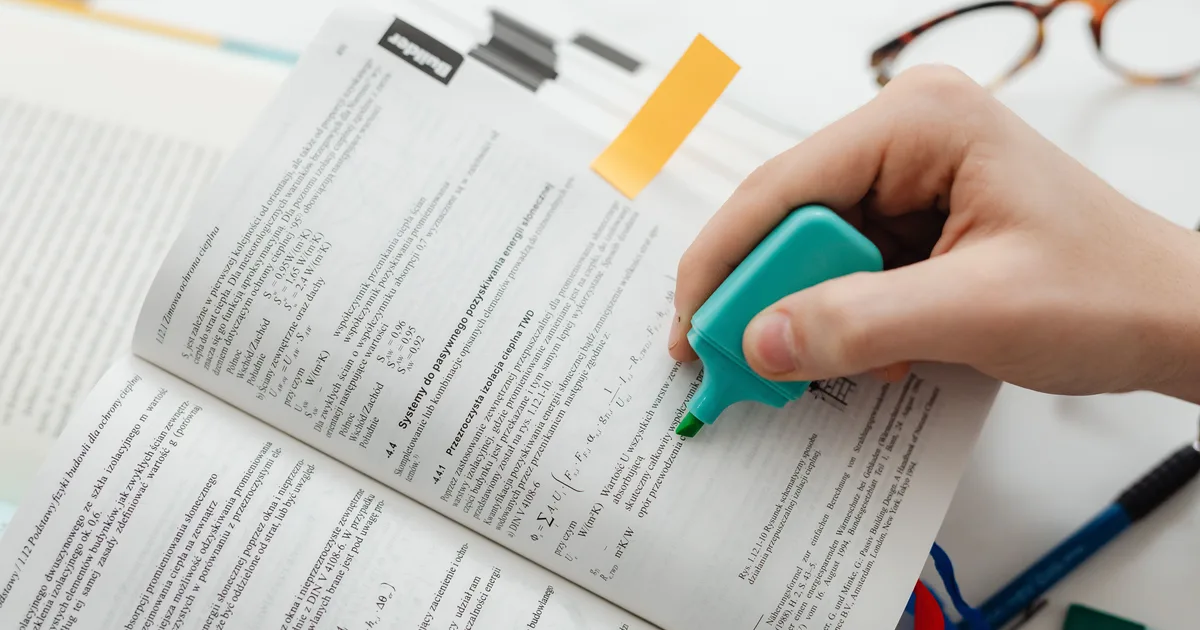 A hand running a highlighter across a printed textbook page, the manual version of what name extraction rules in natural language processing do to text