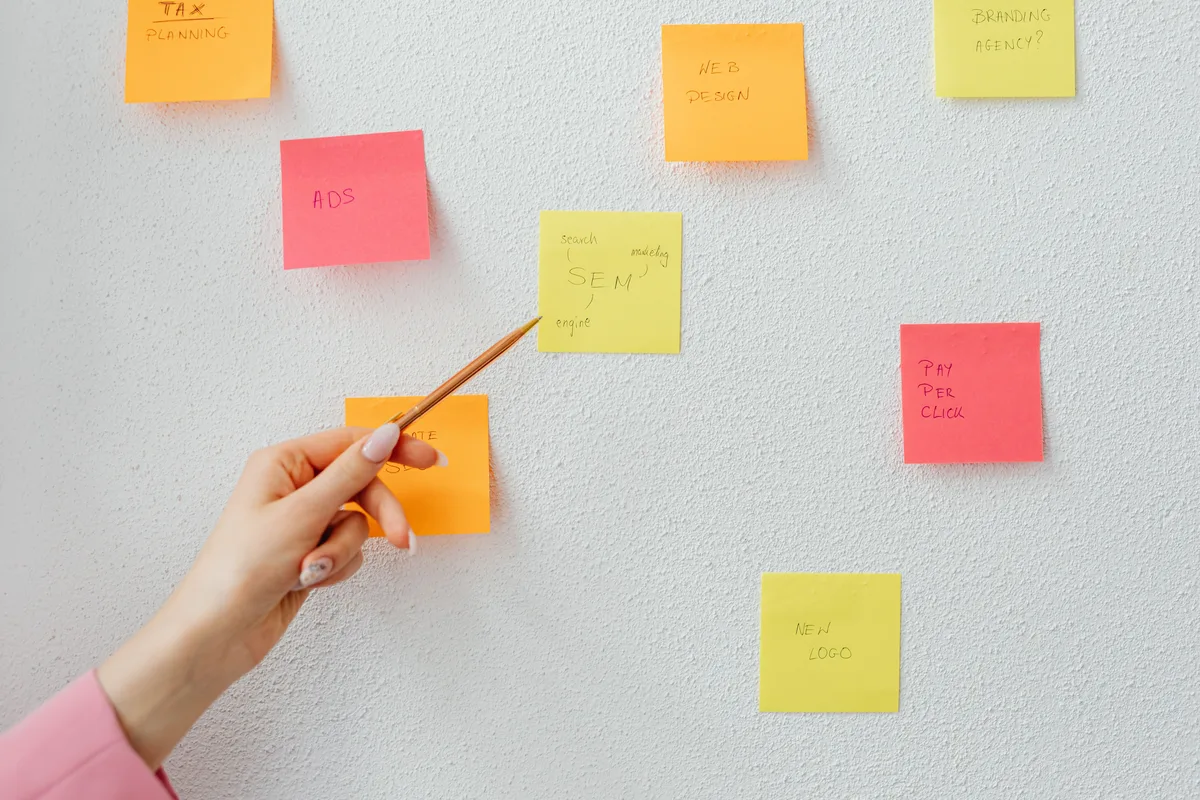 A hand pointing at colourful sticky notes on a wall, the competing hypotheses a prompt to help for AI discovery should surface