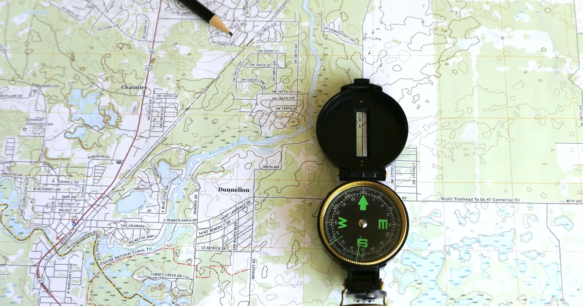 A detailed topographic map with a compass and pencil resting on it, the survey a prompt to help for AI discovery is meant to produce