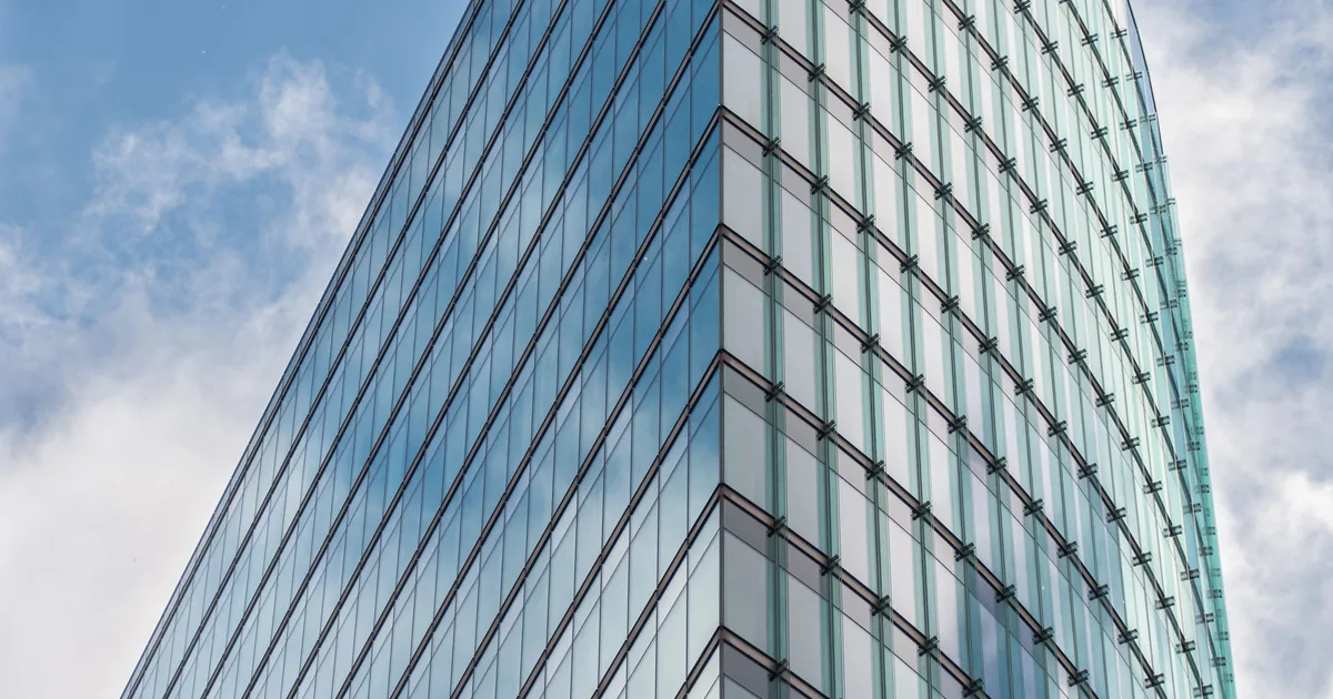 Glass skyscraper reflecting a blue sky, standing in for the corporate question of who owns Claude AI