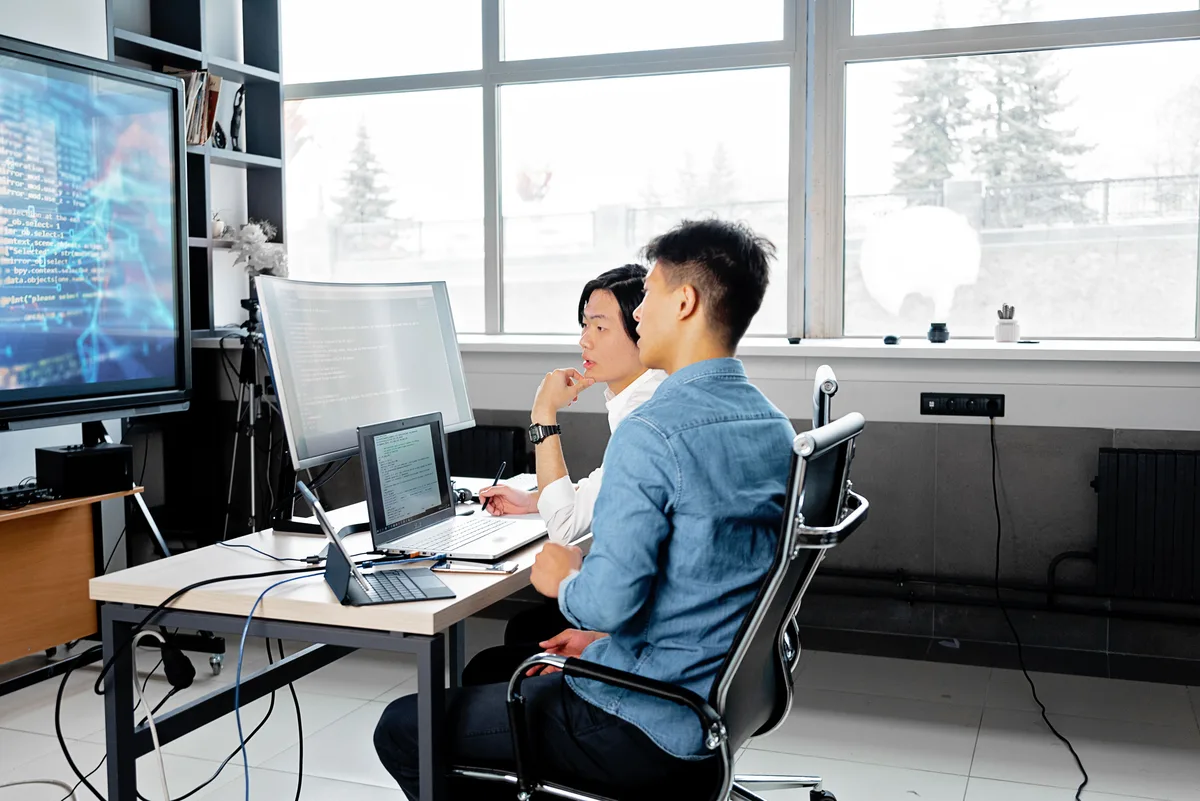 Two engineers reviewing code together on separate monitors in an office